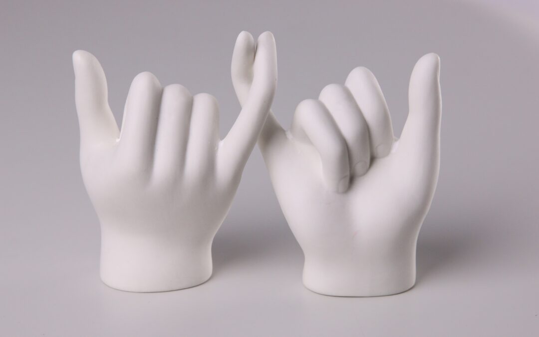 A white sculpture of two hands with intertwined pinky fingers.